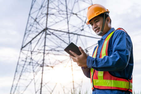 Asian electrical engineer wear safety clothes standing and watching at the electric power station to view the planning work by producing electricity at high voltage electricity poles.の写真素材
