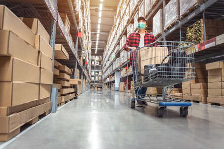 Asian man wearing a shopping mask in Rows of shelves with goods boxes in modern industry warehouse store at factory warehouse storage to decorate the houseの写真素材