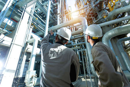 Industrial engineer or worker checking pipeline at oil and gas refinery plant form industry zone with sunrise and cloudy sky, oil and gas Industry concept.の写真素材