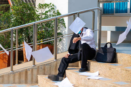 Asian businessman throw a job application and stress sitting on stair, are worrying about unemployment, concept unemployment problem.の写真素材