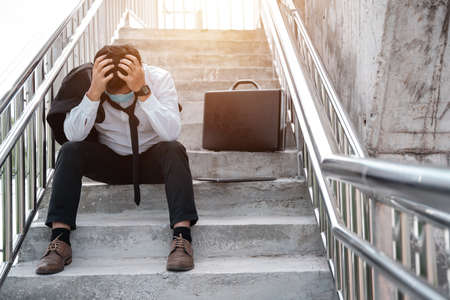 Unemployed stressed young Asian business man in suit covering face with hands. Failure and layoff concept to the disease Covid-19,Work and stress. business people despair low economic crisisの写真素材