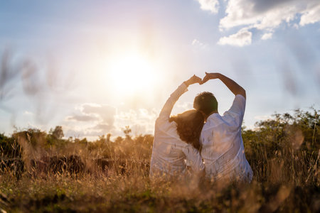 Happy romantic couple the sunset in the meadow love gesturing a heart with arm.の写真素材