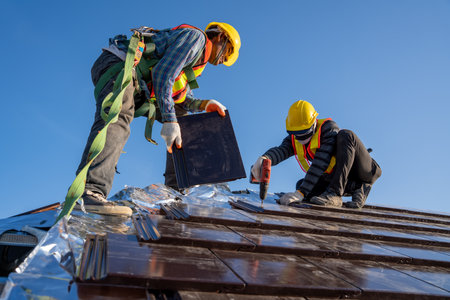 Two work construction worker install new ceramic tile roof with Roofing tools electric drill used in the construction site.の写真素材