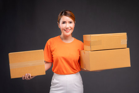 Delivery asian woman or courier wearing an orange uniform holds a cardboard box in studio.