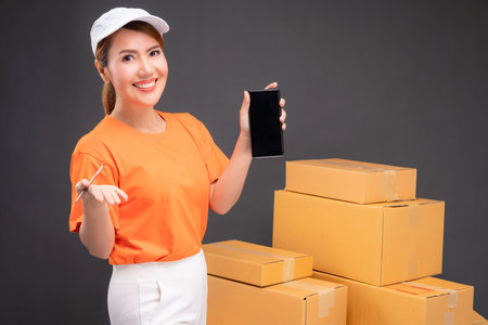 Online shopping with a smartphone start small business in a cardboard box at work. Asian female...