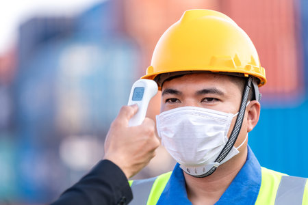 Close up asian worker scanning fever temperature with digital thermometer to industry construction site staff wearing hygiene face mask protect from Coronavirus or COVID-19. New Normalの写真素材