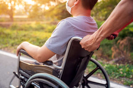 Close up hand patient or disabled man is sitting in wheelchair and young son on a walk in spring nature.の写真素材