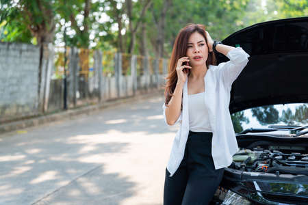 Asian business woman using a mobile phone to call the mechanic while looking at broken down car on street.の写真素材