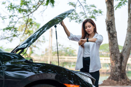 Asian business woman she opened the hood Broken car on the side See engines that are damaged or not  and  watch the time and wait the mechanic.の写真素材