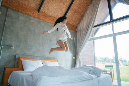 attractive asian woman jumping on bed in the morning, in the morning, She felt very refreshed, natural window light.の写真素材