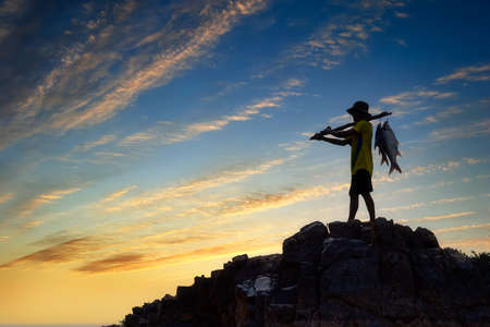 Silhouette Fisherman carrying fish on a rock at sunset. Fisherman in Mekong River, Thailand.の写真素材