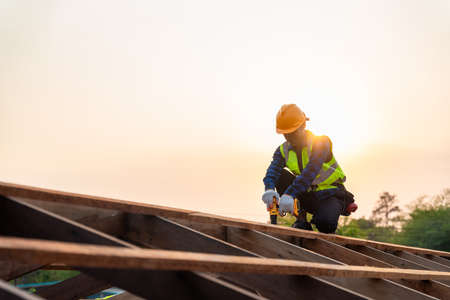 Asian roofer working on roof structure of building on construction site, Roofer using air or pneumatic nail gun and installing on wooden roof structure.の写真素材