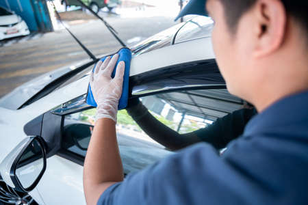 Car detailing - the asian man in uniform holds the microfiber in hand and polishes the car. Selective focus.の写真素材