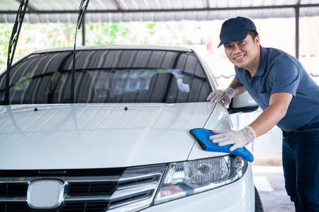 happy asian man in uniform holds the microfiber in hand and polishes the car, Car wash service concept.の写真素材