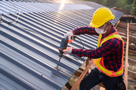 Top view Construction worker safety wear using electric drill tools install on new roof metal sheet,...