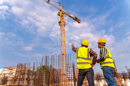 Construction engineers and  architect supervising progress of building construction project stand on...