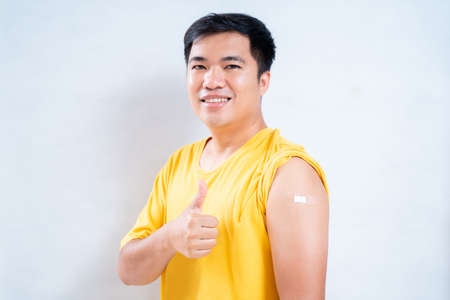 Happy asian man in the shoulder with plaster on arm after vaccination on a white background, Concept of vaccination against the coronavirus or COVID-19の写真素材