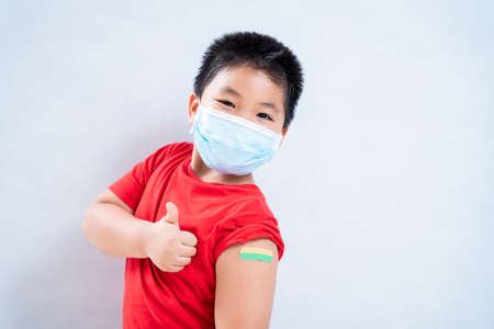 Happy asian boy or child wearing a mask in the shoulder with plaster on arm after vaccination on a white background, Concept of vaccination against the coronavirus or COVID-19の写真素材