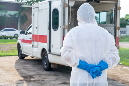 Frontline doctor wear PPE in front of the ambulance with protective suit, mask gloves at ambulance car vehicle for an ambulance carrying the body of the dead from the coronavirus disease COVID-19の写真素材