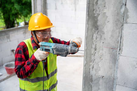 tiler using electric impact drill to drilling cement wall at unfinished house constructionの写真素材