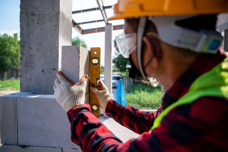 Close-up bricklayer builder  using the water level, check the inclination of autoclaved aerated concrete blocks. Walling, installing bricks on construction siteの写真素材