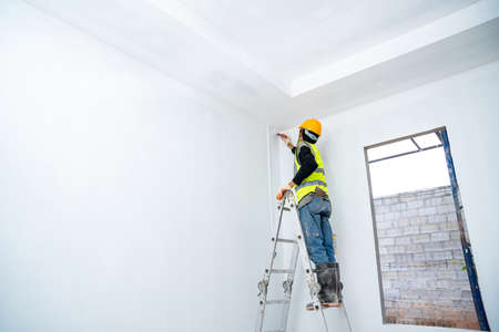 painter man painting the wall in an unfinished building, with paint brush and bucket, isolated on big empty space with ladder at the construction siteの写真素材