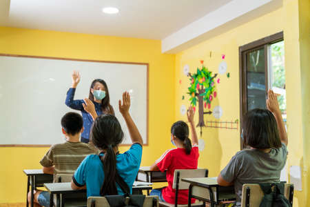 Asian teacher with face mask welcoming children back at school after lockdown.の写真素材