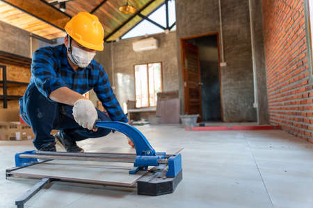 Select focus floor tile cutting equipment, Asian artisan tiler at construction site, worker cuts a large slab of tile during the construction of a houseの写真素材