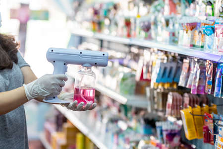 close up hand of staff wearing gloves using electric Alcohol Nano Spray Gun Handhold Blue Light Disinfectant Spray. prevent infection Covid-19 in the shop. concept healthcarの写真素材