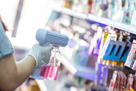 close up hand of staff wearing gloves using auto gun for spraying disinfectant in the shopの写真素材