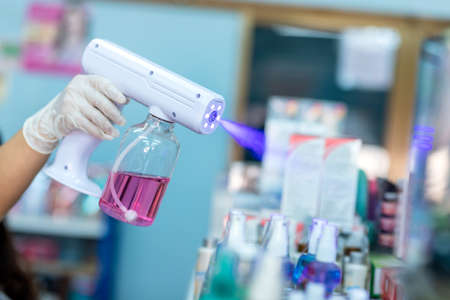 close up hand of staff wearing gloves using electric Alcohol Nano Spray Gun Handheld Blue Light Disinfection Spray Gun Fogging Machine Sanitizer Atomizer in the shopの写真素材