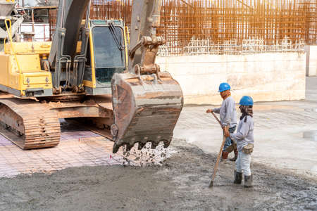Construction worker with excavator heavy machine for Concrete pouring during commercial concreting floors of building at construction siteの写真素材