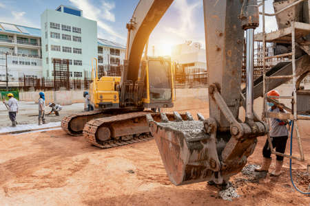 A construction worker with excavator heavy machine and cement truck for pouring a wet concret at building construction siteの写真素材