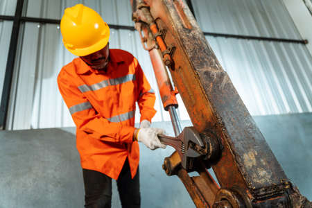 A technician working excavator repair with large iron wrench in a hand, Powerful Professional Mechanic. Heavy Duty Equipment Maintenance. Industrial Concept.の写真素材