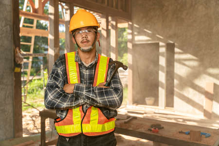 Asian craftsman with holding a hammer in hands standing in spacious workshop and looking at camera on construction siteの写真素材