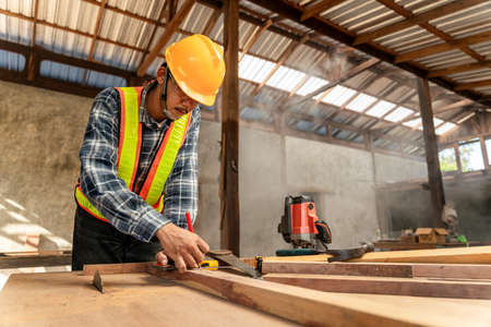 A male carpenter using pencil on a piece of wood on construction siteの写真素材