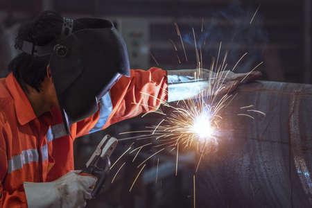 Industrial worker with protective mask labourer at the factory welding steel pipeの写真素材