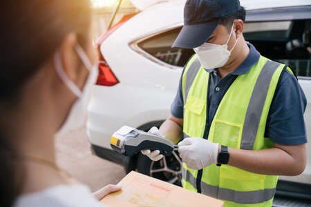 Asian delivery man using a credit card reader while delivering products to customers at home, delivery destination.の写真素材
