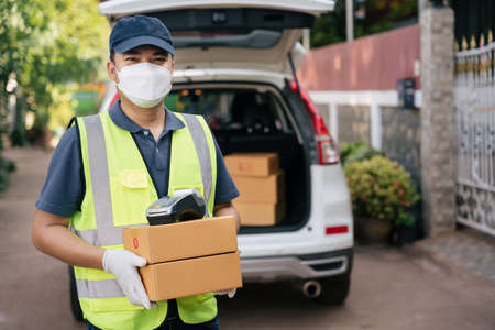 Happy delivery man holding boxes and credit card reader wearing masks to prevent the spread of coronavirus or COVID-19の写真素材