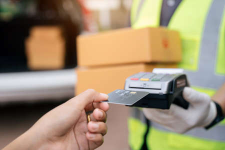 Close up of hand delivery man using credit card swiping machine to pay. Hand with creditcard swipe through terminal for payment on the outside of the warehouse, Select focus credit card.の写真素材