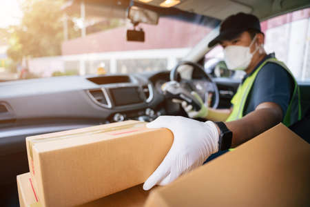 A delivery man holding credit card reader is picking up a box in a friend's car to deliver it to a...