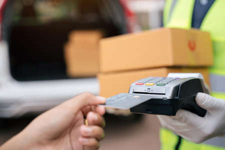 Close up of hand delivery man using credit card swiping machine to pay. Hand with creditcard swipe through terminal for payment on the outside of the warehouse.の写真素材