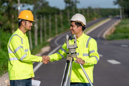 Two surveyor engineers worker handshake after making measuring with theodolite instrument equipment during construction road works success, Civil Engineers, Surveyor equipment.の写真素材