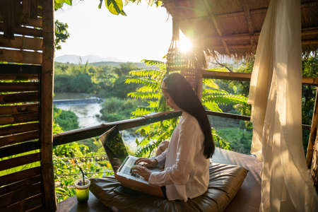 Freelancer woman sitting and writing on the laptop during vacation holidays in summer among the trees and mountains. female blogger.の写真素材