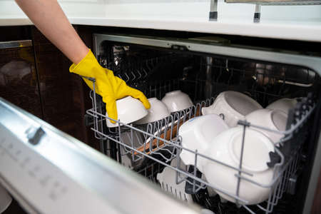 hand of woman arranging plates in dishwasher in the kitchen. maidの写真素材