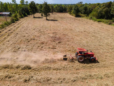Aerial view of Tractor as pulling round baler, machine that rolls up the straw and spits out a packed bale over agricultural field. animal feedの写真素材