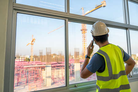 Architect or Engineer inspects the job site and works with a mobile phone, Crane on the construction site background.の写真素材