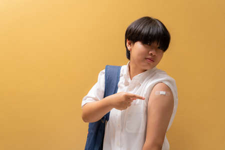 Asian happy girl index finger to shoulder and showing her arm with bandage after got vaccinated in student uniform, teenager immunization, Covid preventive vaccine.の写真素材