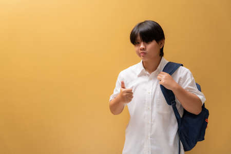 Asian girl giving wear a protective mask with thumb up and learning equipment in student uniform, Education concept and prevention of the spread of corona virus.の写真素材
