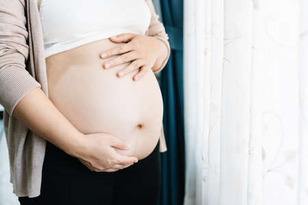 Close up of pregnant woman with big belly at window. pregnancy, motherhood, people and expectation concept. mother.の写真素材